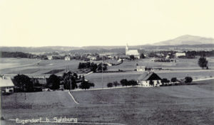 Eugendorf gegen Norden, um 1930: Im Vordergrund links der Strasserwirt, im Mittelgrund die Trasse der ehemaligen Salzkammergutlokalbahn mit dem kleinen Bahnhofsgebäude (Reproduktion: SLA)